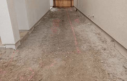 Construction site with marked pathway and gravel, leading to a wooden gate entrance.