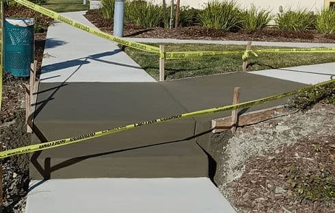 Freshly poured concrete sidewalk with caution tape and wooden framing for safety.
